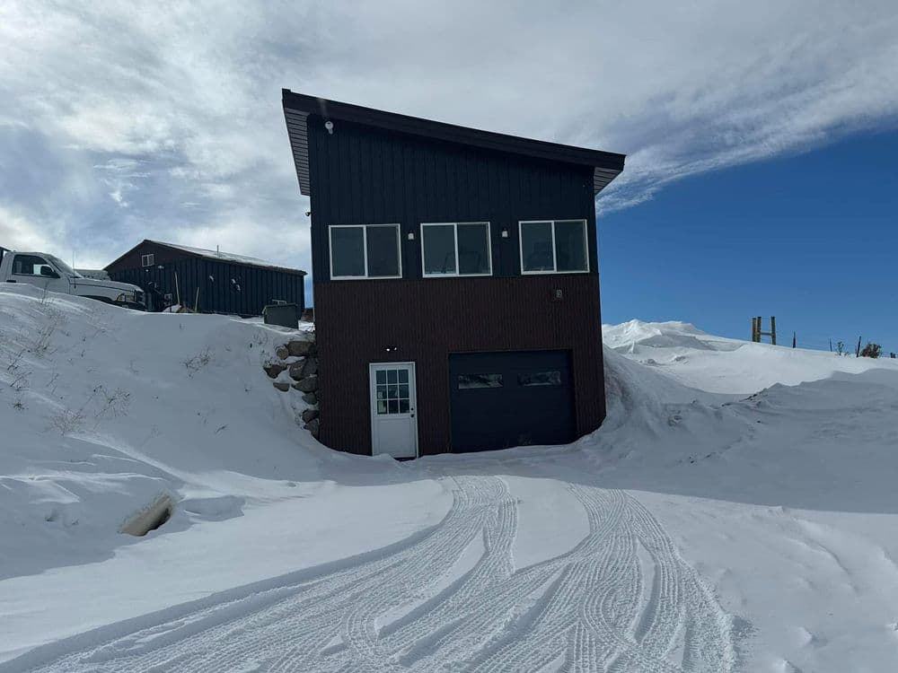 Modern two-story building surrounded by snow under a blue sky with visible tire tracks.