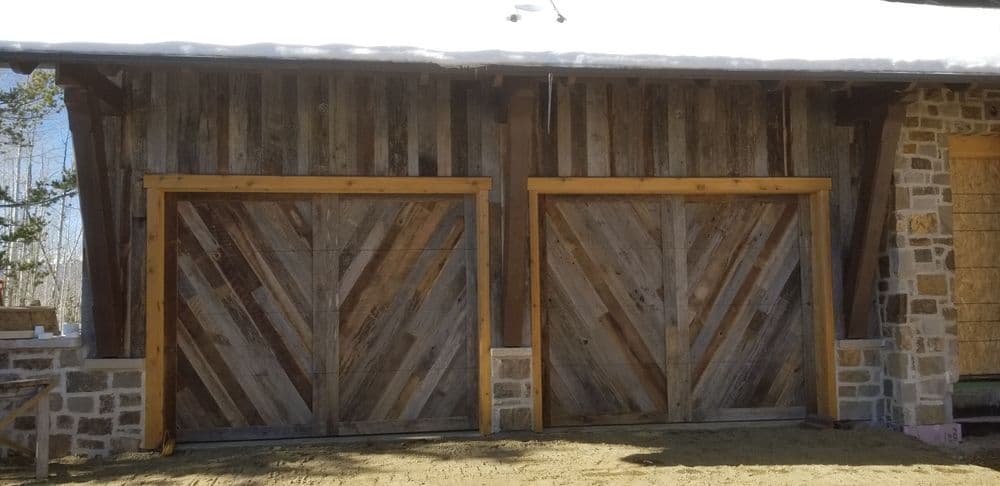 Rustic wooden barn doors with diagonal patterns on a cabin in a snowy landscape.