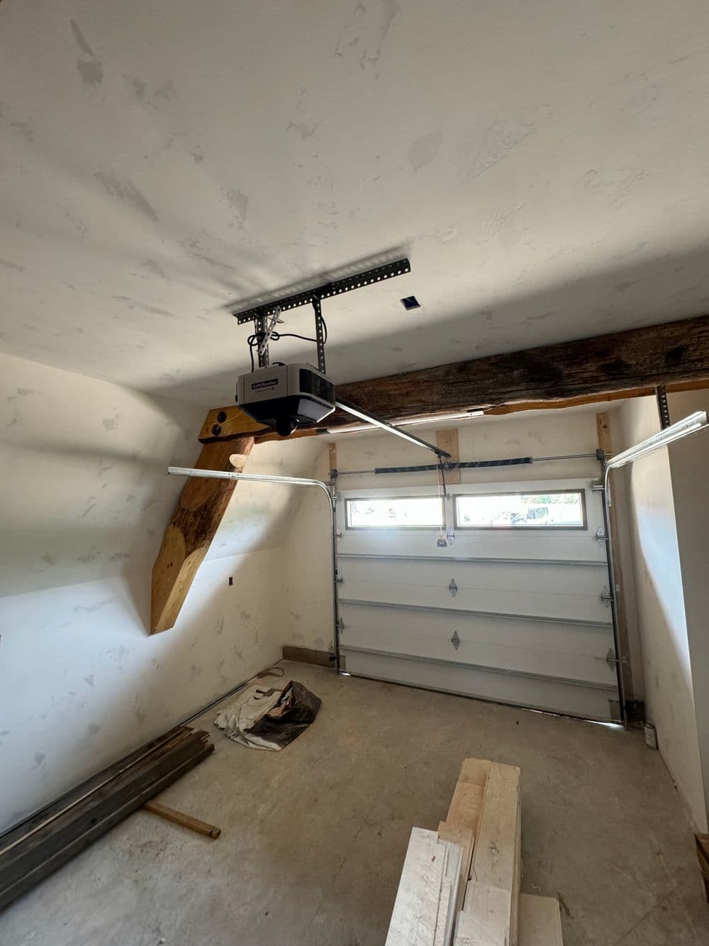 Garage interior featuring wooden beams and a garage door opener. Construction materials visible.