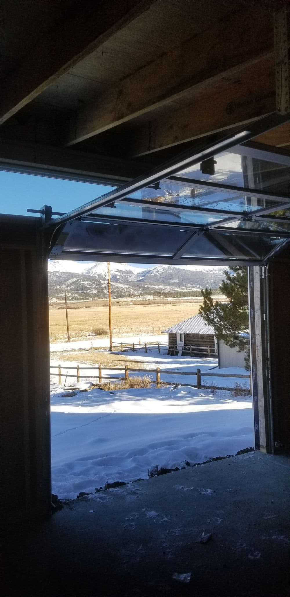 View from a garage doorway revealing snowy landscape and mountains in the background.