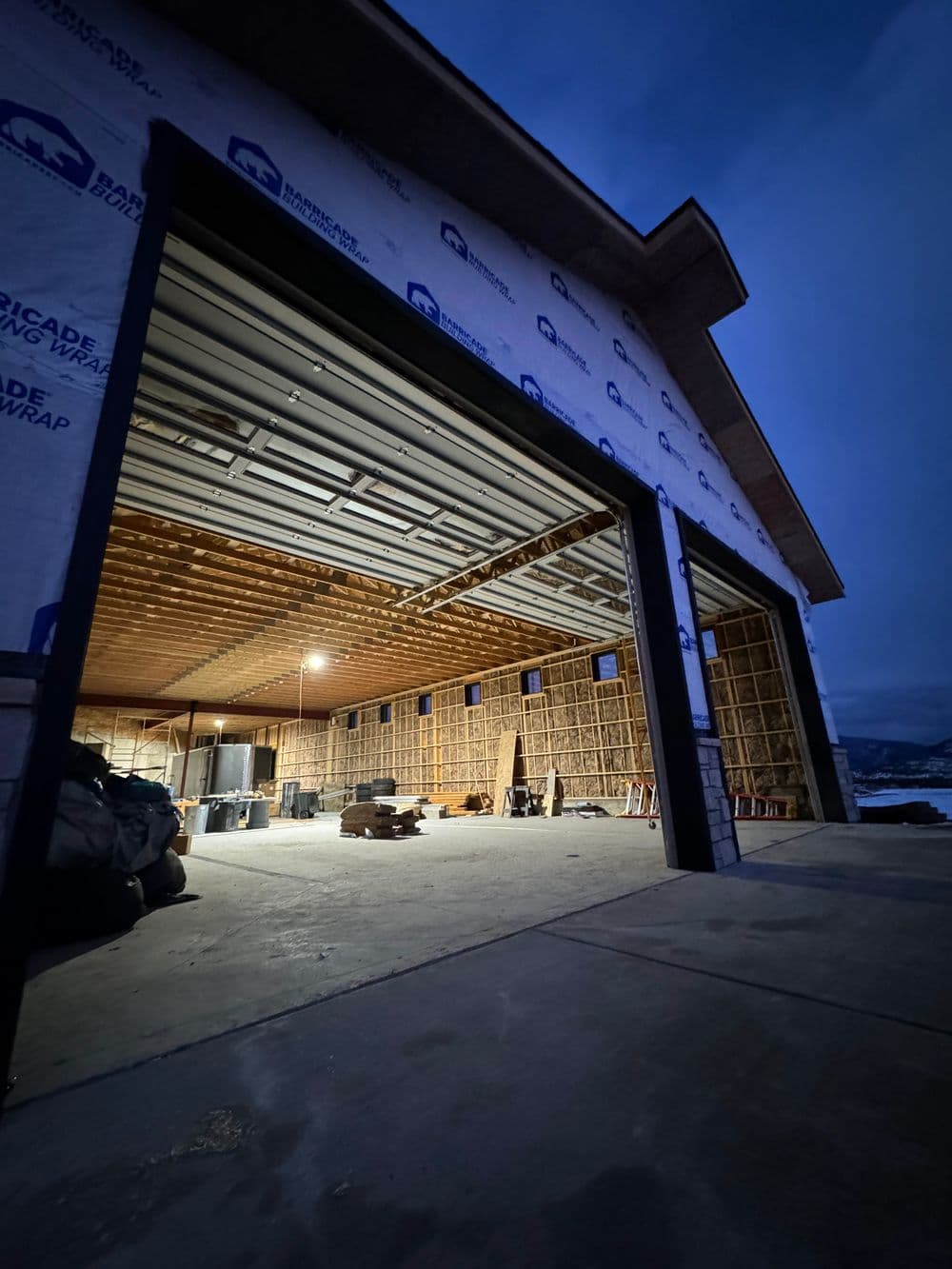 Spacious garage interior at dusk, featuring framing and construction materials.