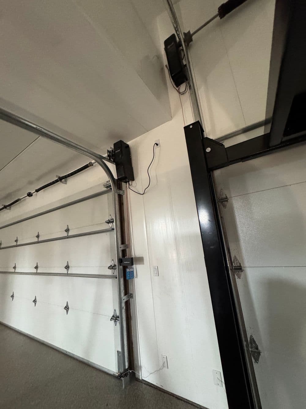 Garage interior showing roller door mechanism and wall-mounted devices.