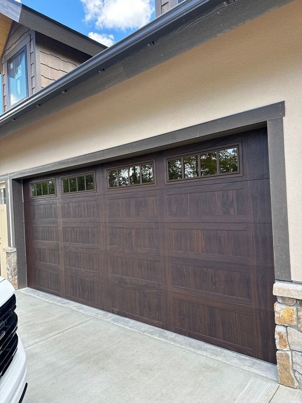 Modern wooden garage door with windows, mounted on a stone and stucco home exterior.