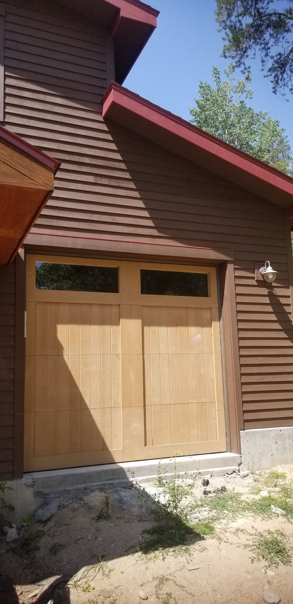 Wooden garage doors on a modern house with brown siding and red roof accents.