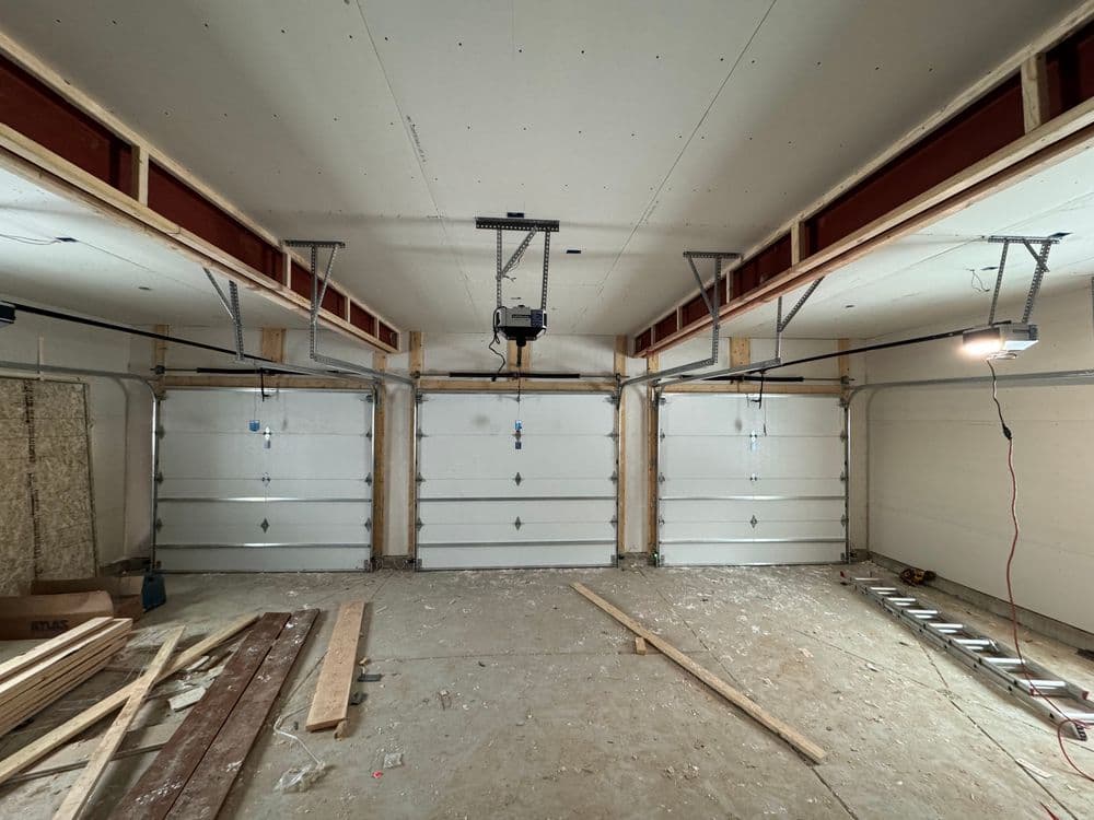 Spacious garage interior with three white doors and construction materials on the floor.