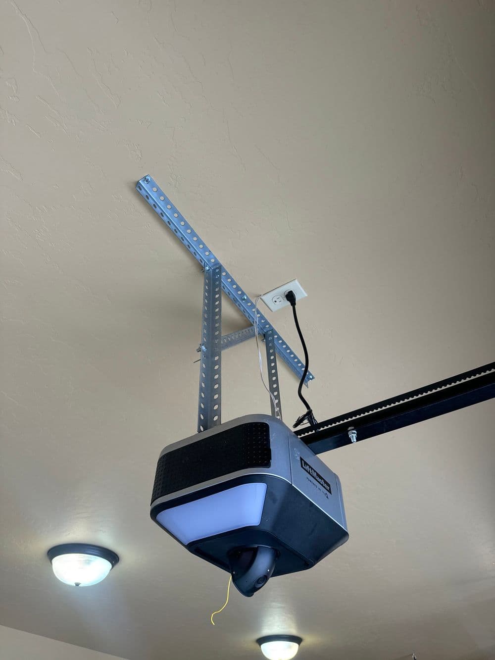 Garage door opener mounted on ceiling with overhead lighting and power connection.