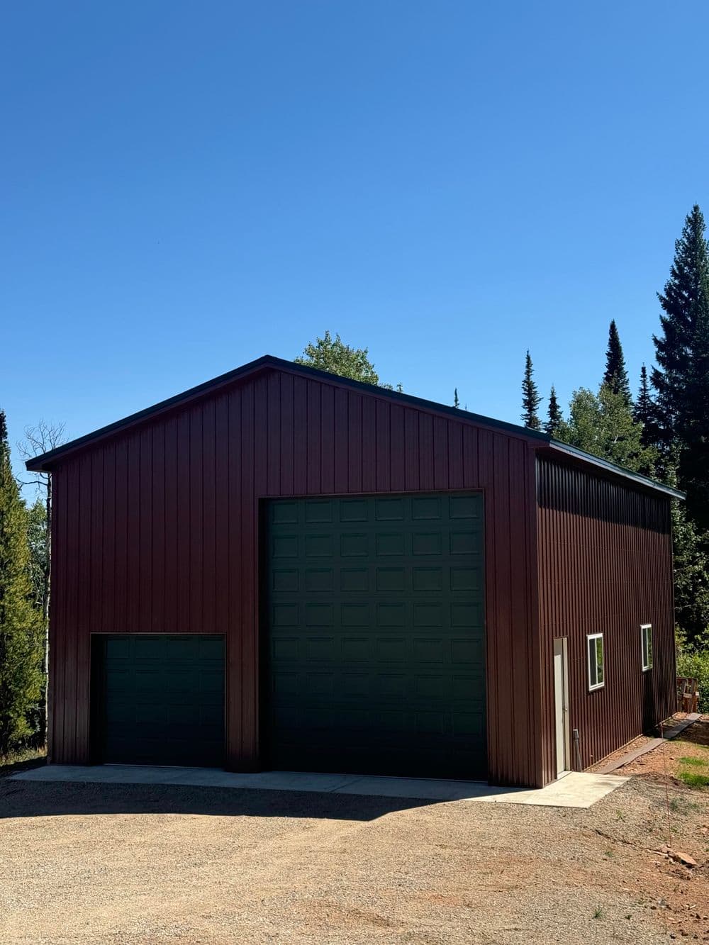 Large brown metal storage building with two garage doors and surrounding trees.