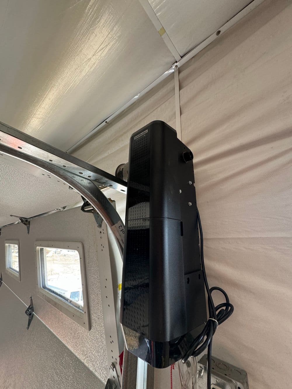 Black projector mounted on a ceiling in a white tent interior, with power cord visible.