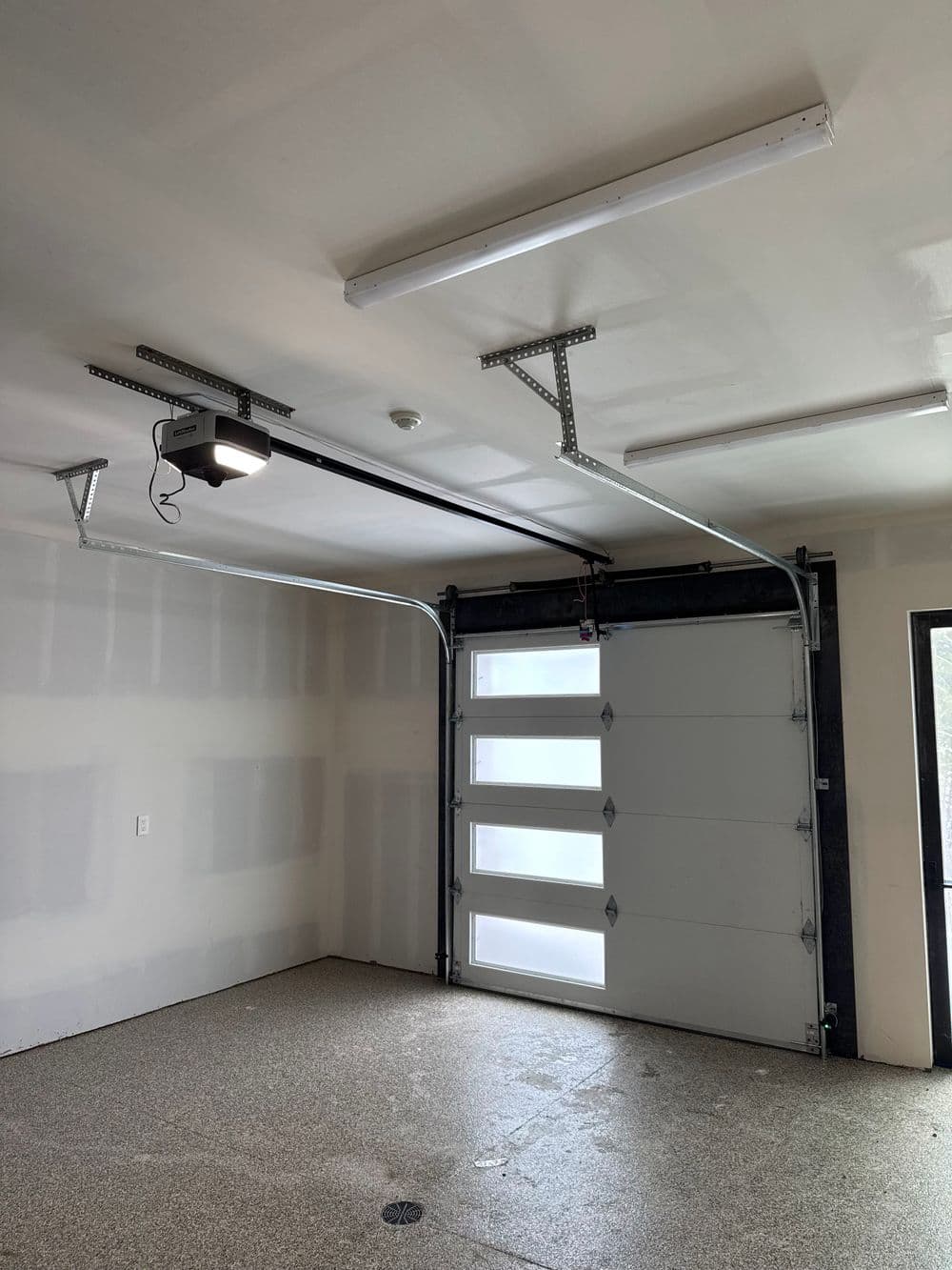 Modern garage interior with overhead lighting and a large garage door. Clean, spacious design.