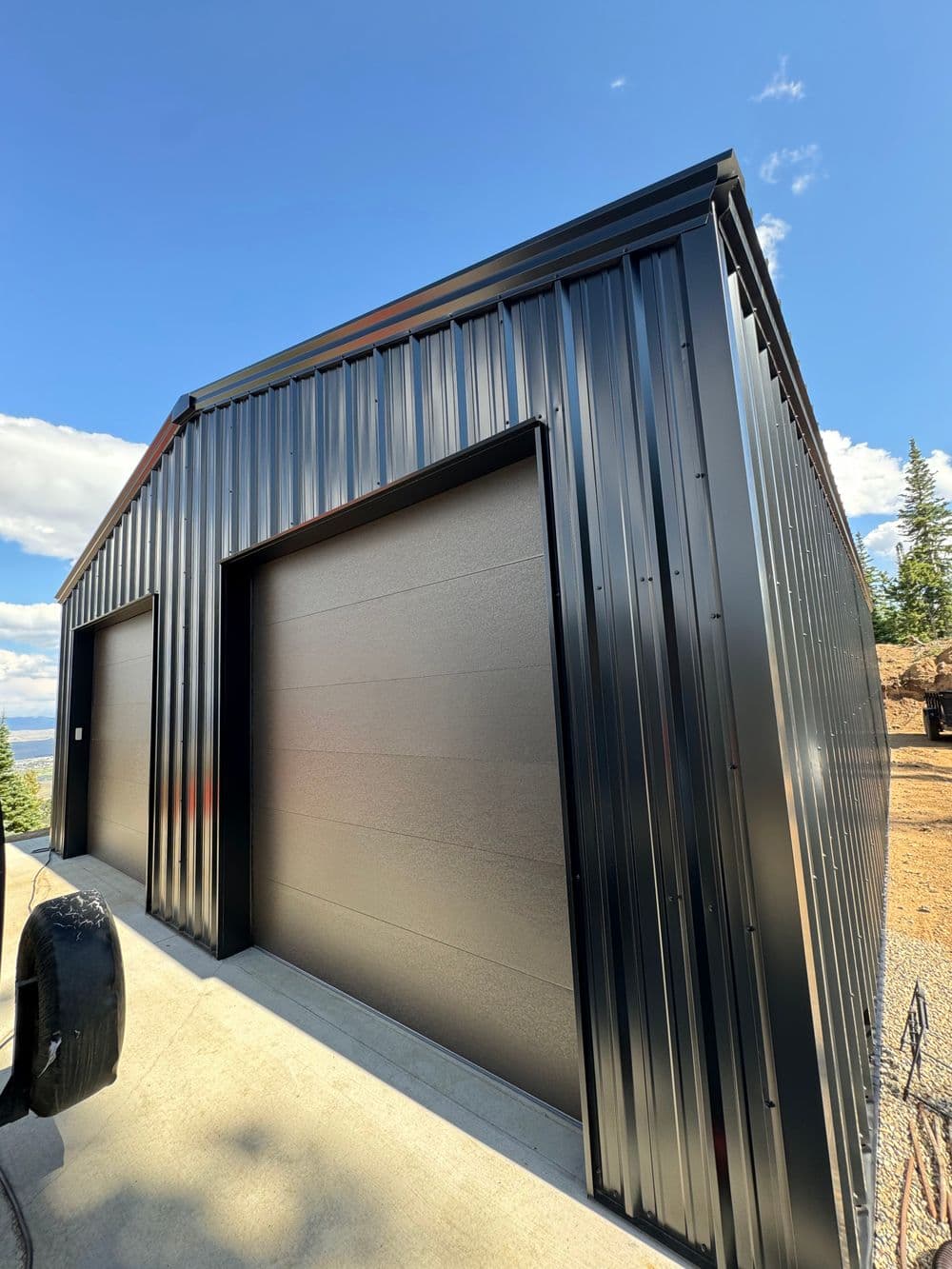 Modern black metal storage shed with large roll-up doors against a clear blue sky.