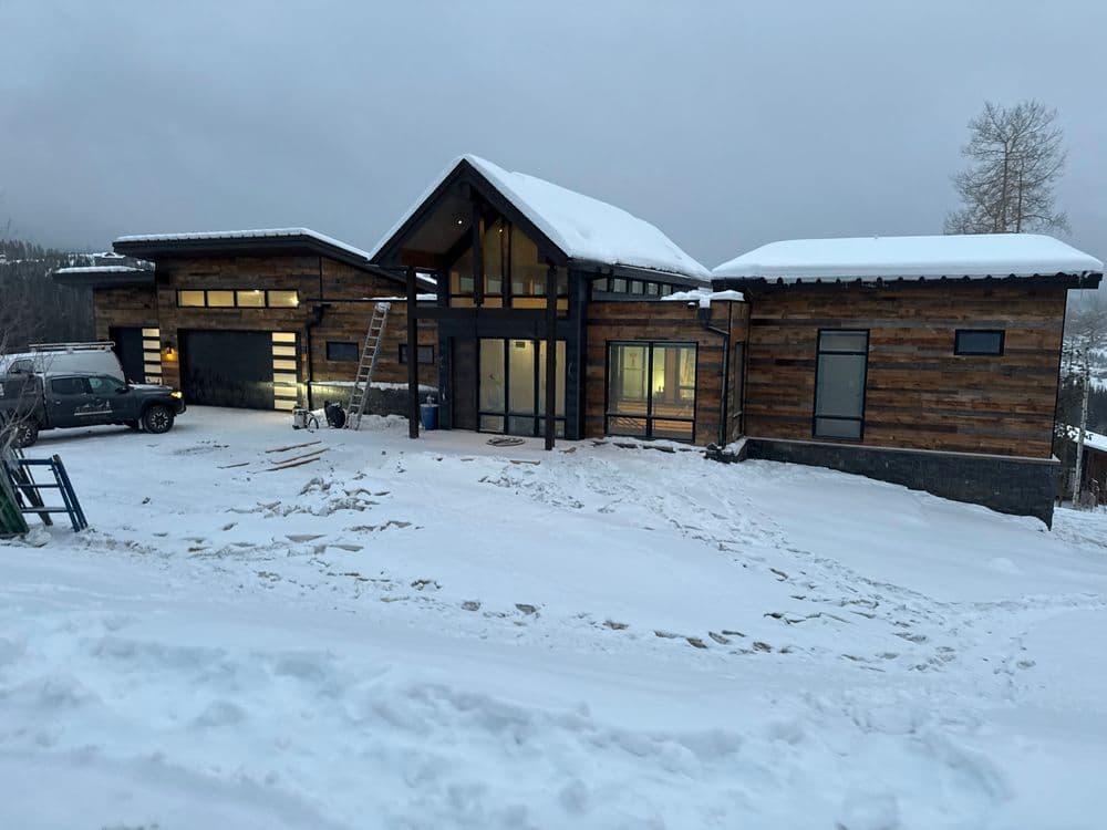 Modern mountain home exterior covered in snow with large windows and wooden accents.