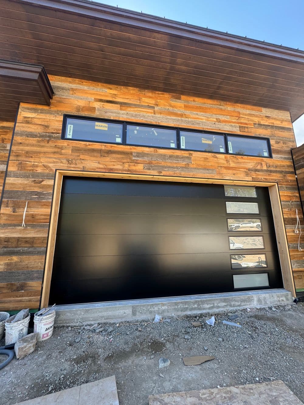 Modern black garage door with wooden accent on contemporary home facade under construction.