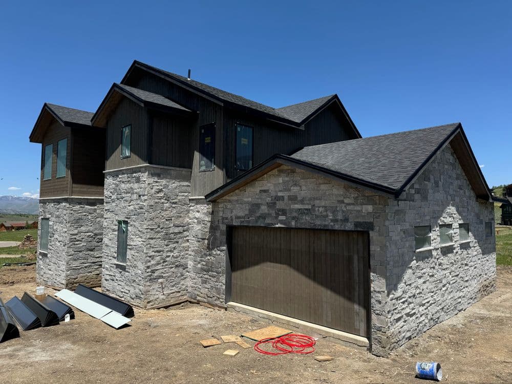 Modern two-story home with stone exterior and garage, set against a clear blue sky.
