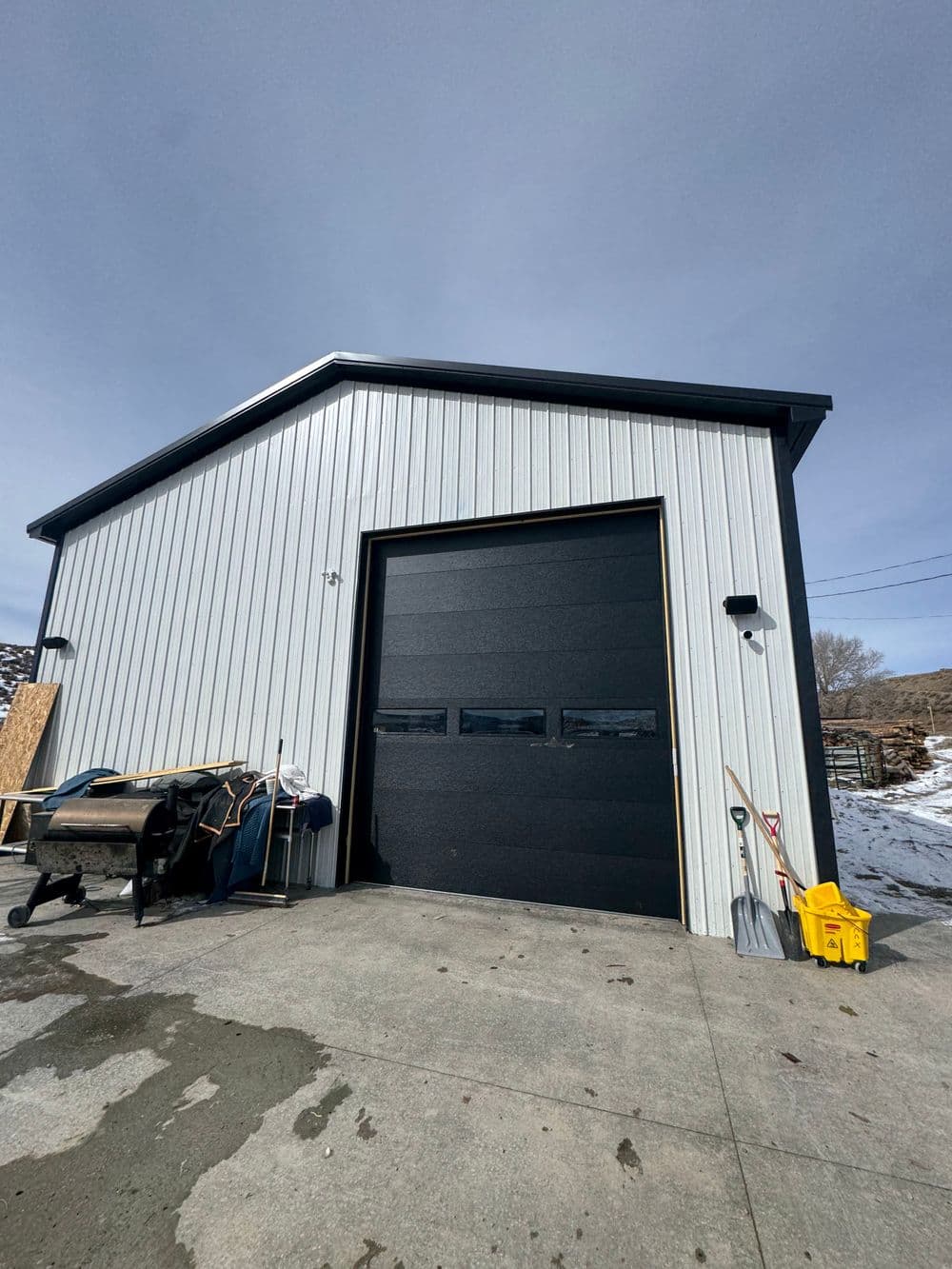 Modern metal garage building with a large black door and snowy surroundings.