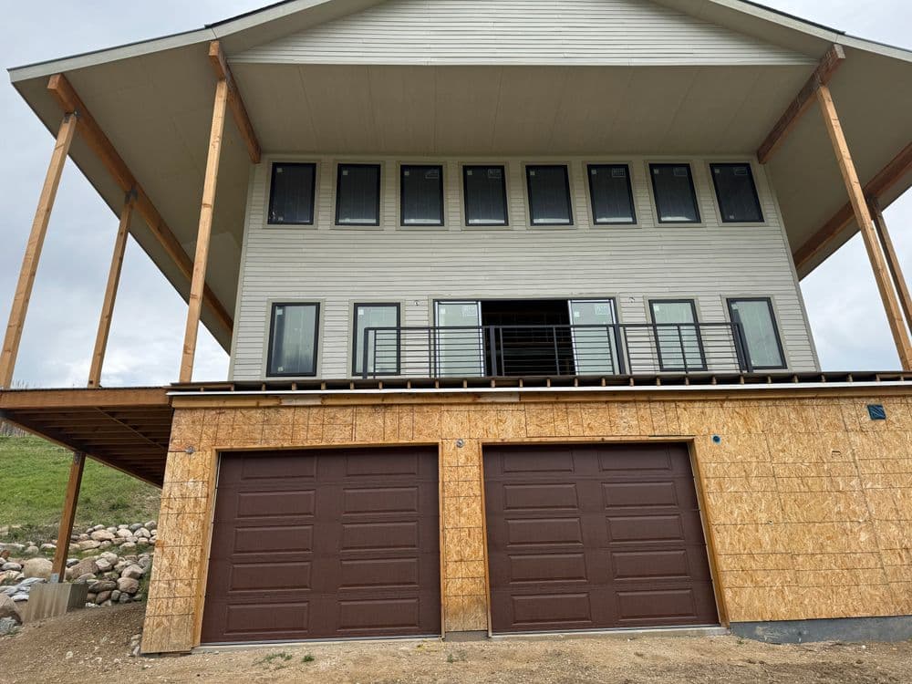 Modern two-story house with large windows and elevated garage, under construction.
