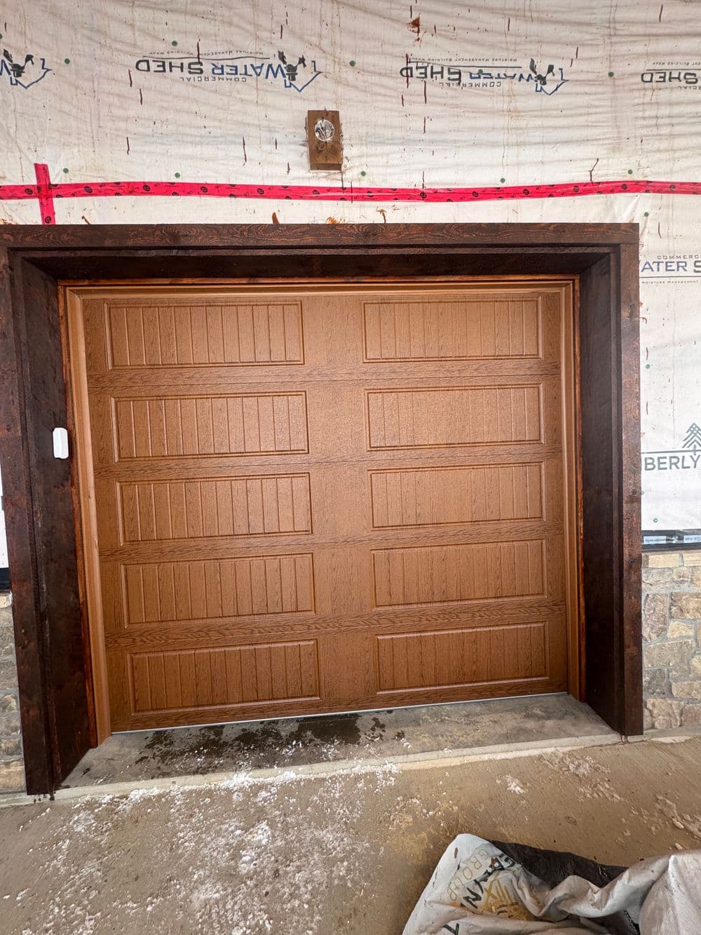 Wooden garage door with panel design in a partially constructed home setting.