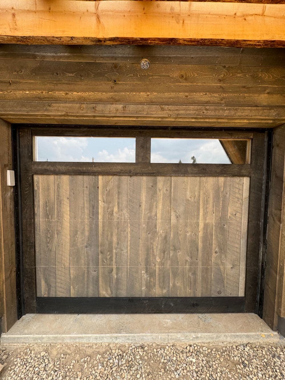 Wooden garage door with glass panel, featuring a rustic design and sturdy metal frame.