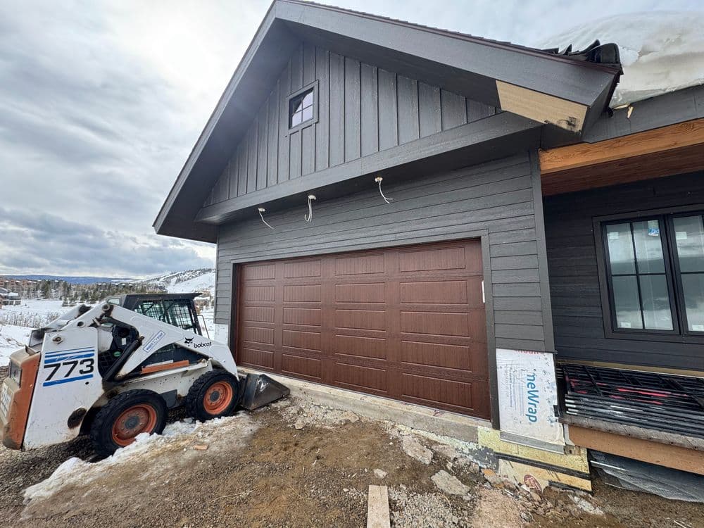 Newly constructed home exterior with brown garage door and construction vehicle on site.
