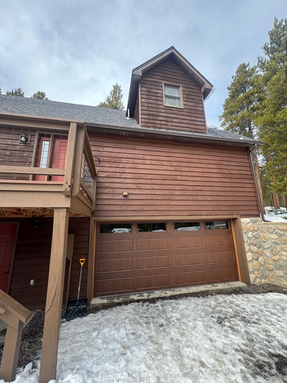 Chalet-style home with wooden exterior and garage, surrounded by snow and pine trees.