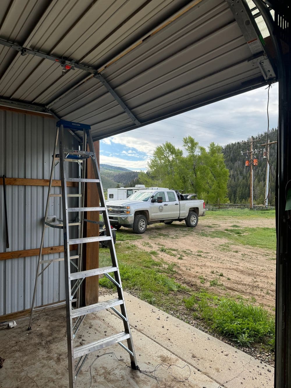 Ladder inside a garage with a truck parked outside and scenic mountains in the background.
