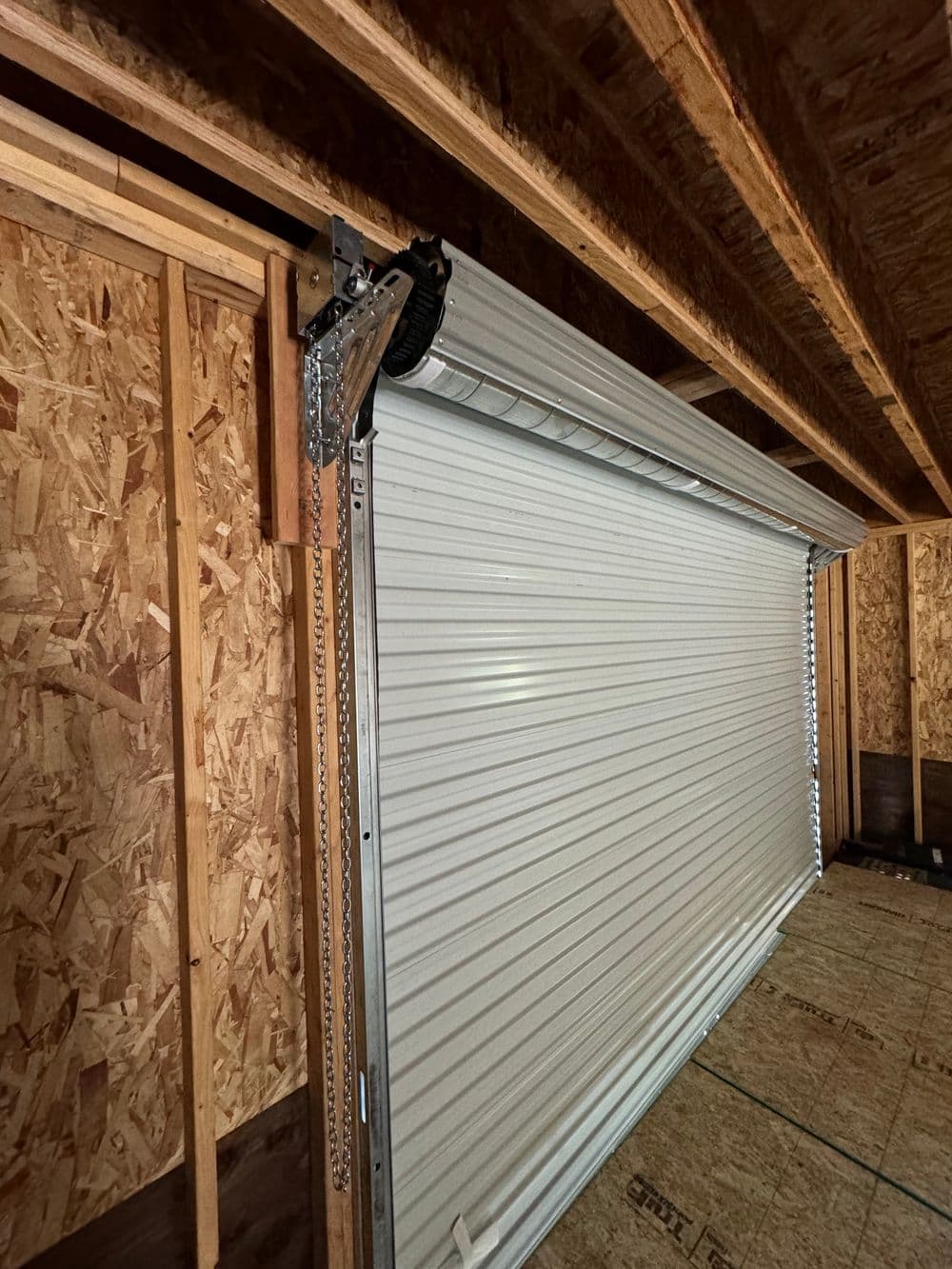 Rolling metal garage door installed in a wood-framed structure with exposed beams.