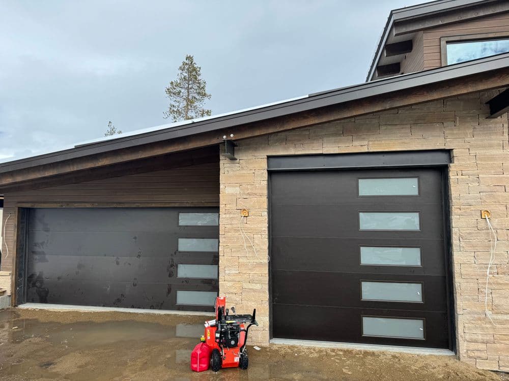 Modern home with two garage doors and a red snowblower in front. Stylish stone exterior.