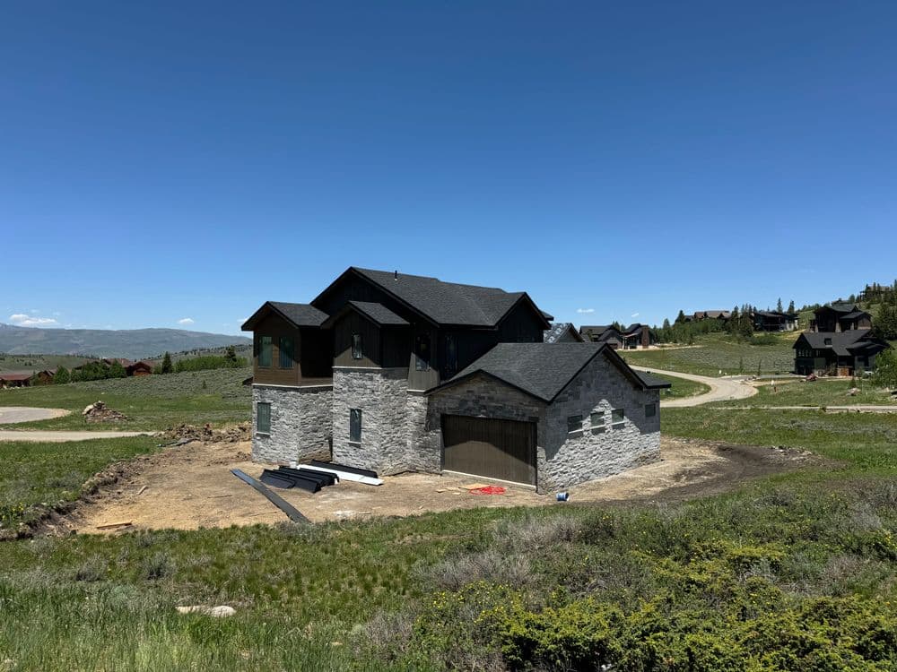 Modern two-story house with stone accents set in a scenic green landscape under a clear blue sky.