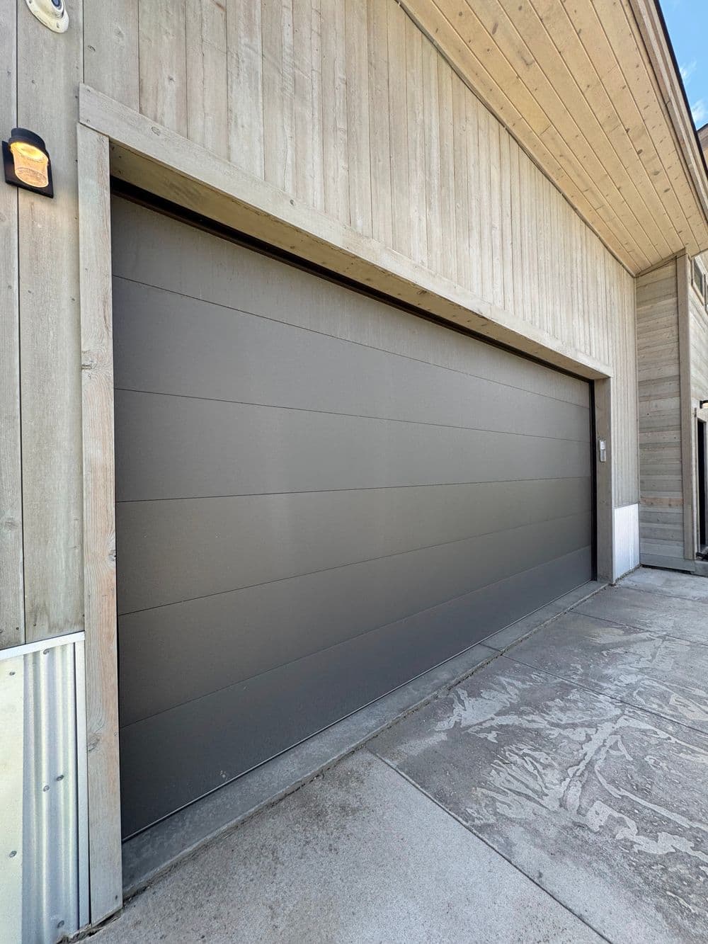 Modern grey garage door on wooden building exterior with concrete driveway.