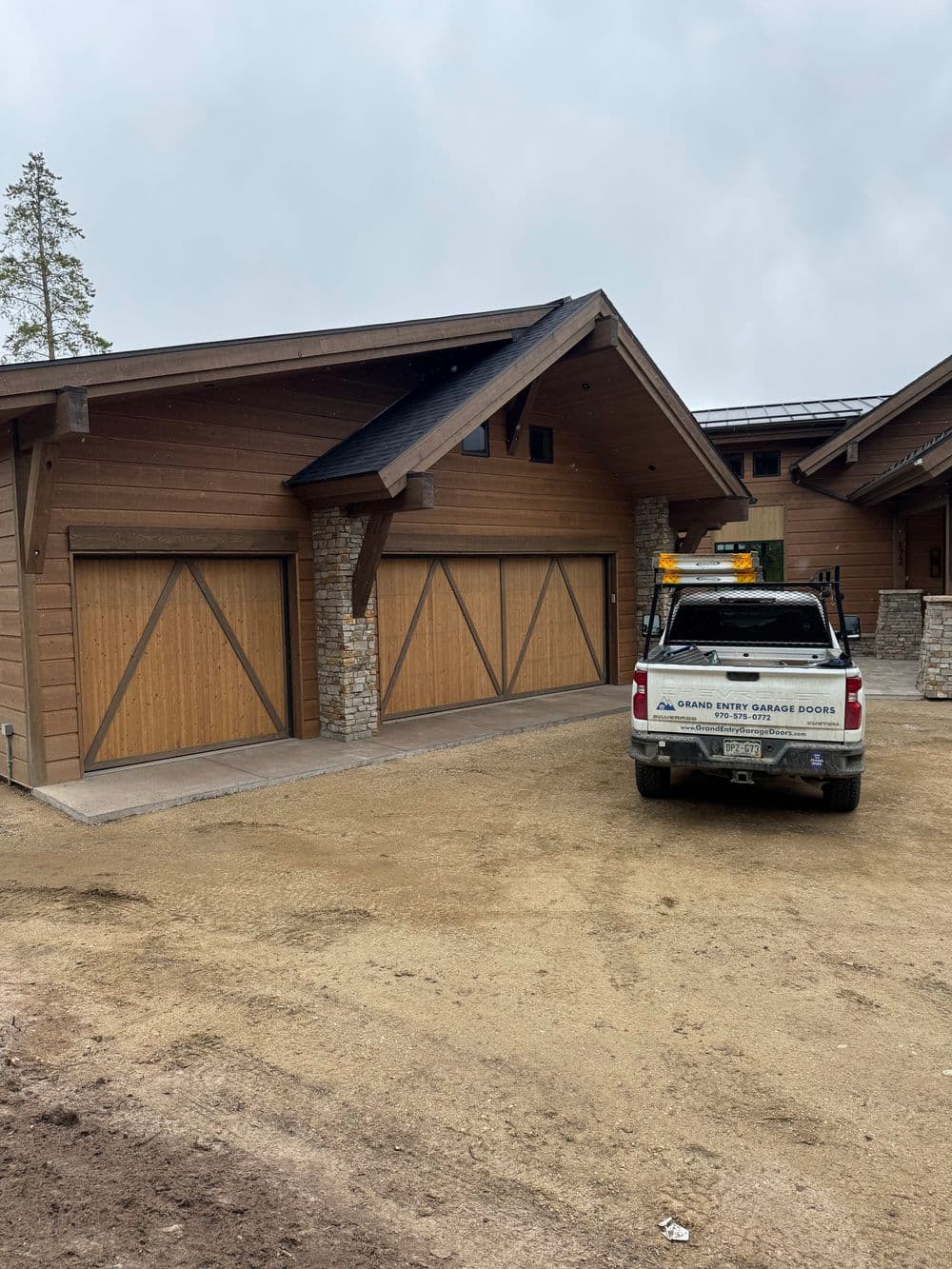 Modern wooden garage doors on a rustic house with a pickup truck parked outside.