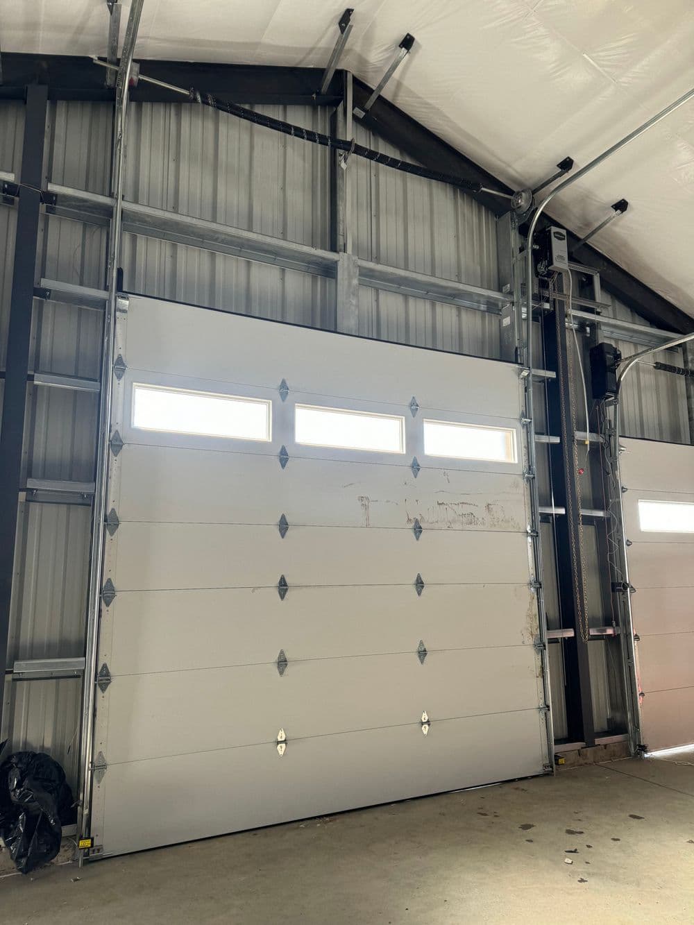 White garage door with windows in industrial setting, featuring metal framework and concrete floor.