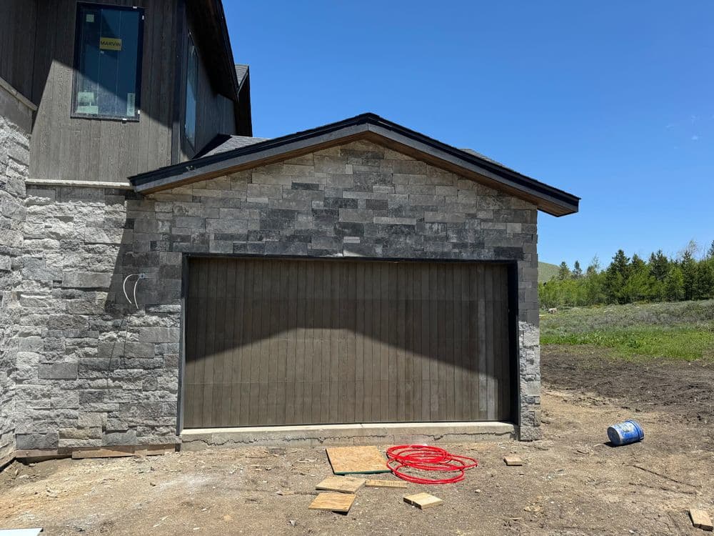 Modern home exterior with stone accents, unfinished garage, and construction materials outside.