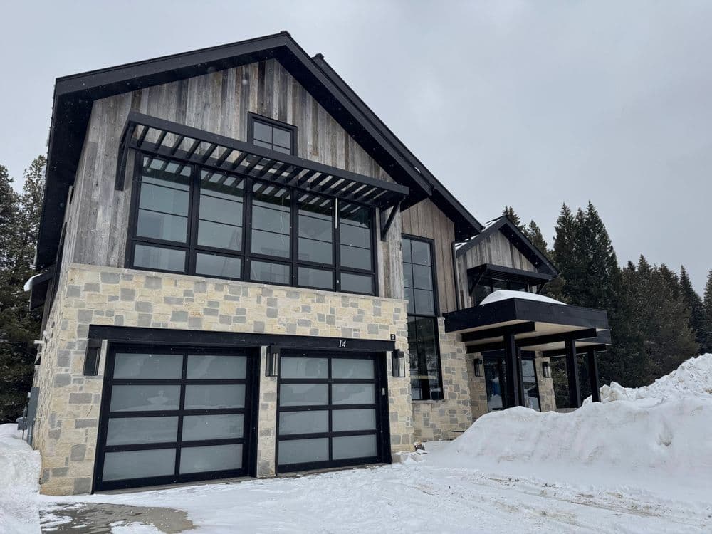 Modern mountain house with large windows and stone exterior, surrounded by snow.