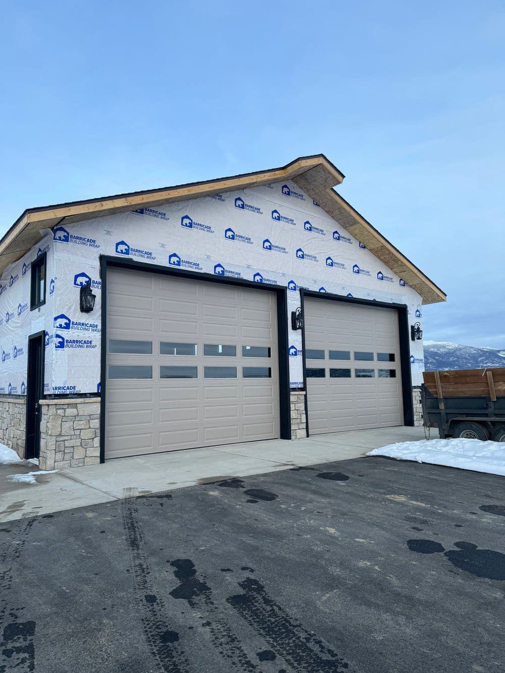 Newly constructed garage with modern double doors, stone accents, and unfinished exterior.