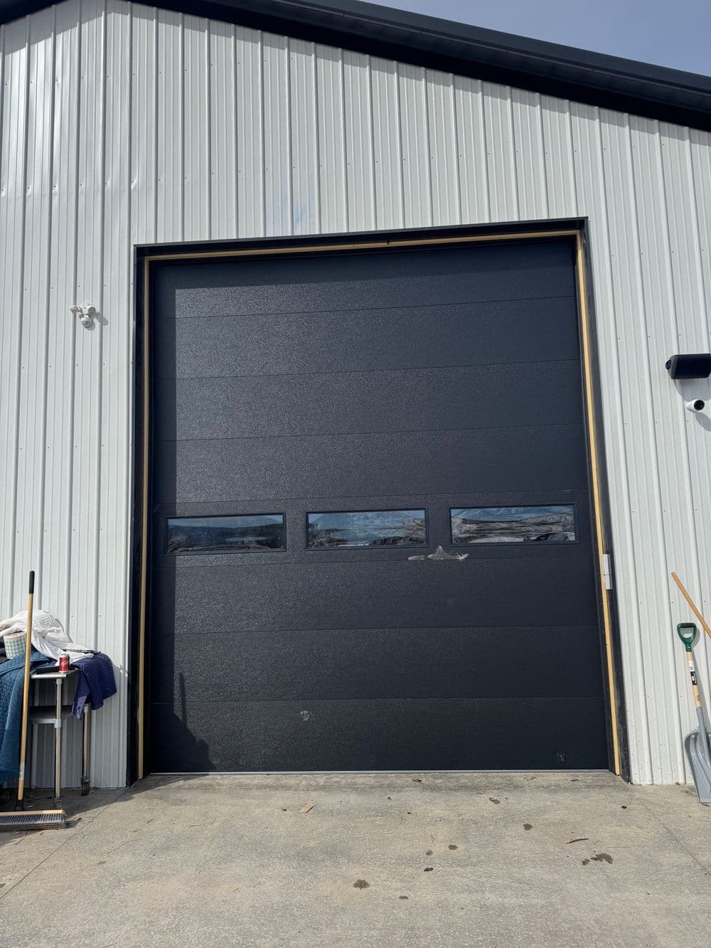 Large black garage door with windows, set against a metal shed exterior. Clean concrete floor.
