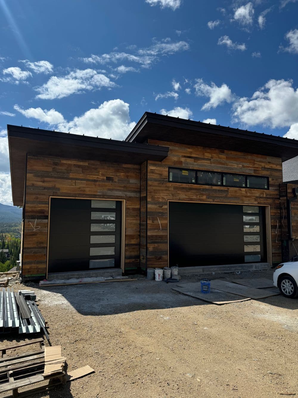 Modern wooden house exterior with large garage doors and scenic backdrop. Construction site.