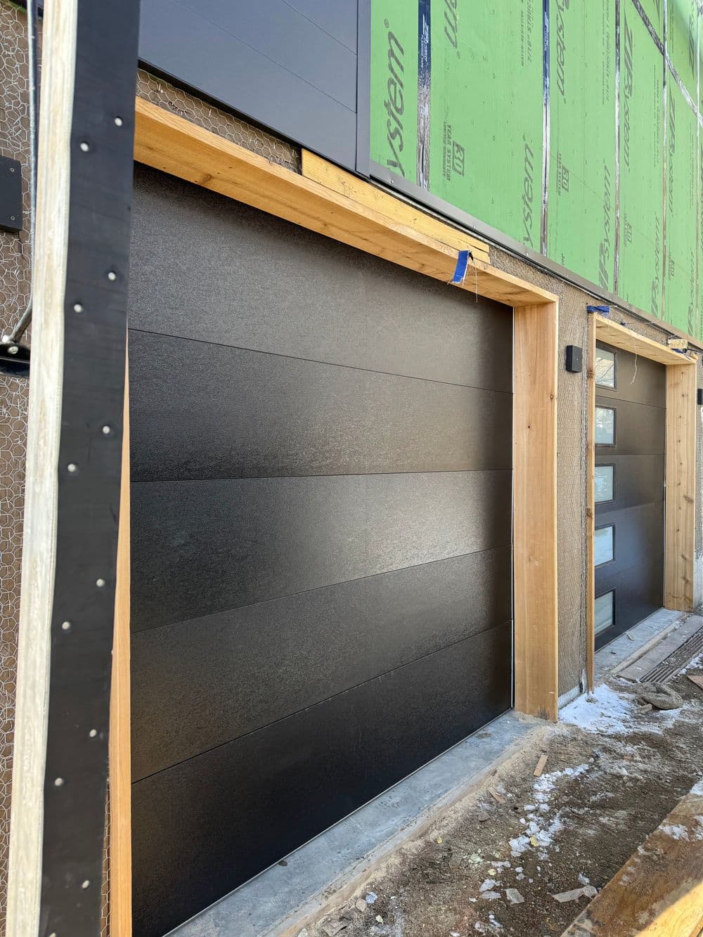 Modern black garage doors with horizontal panels during construction. Wood frame visible.