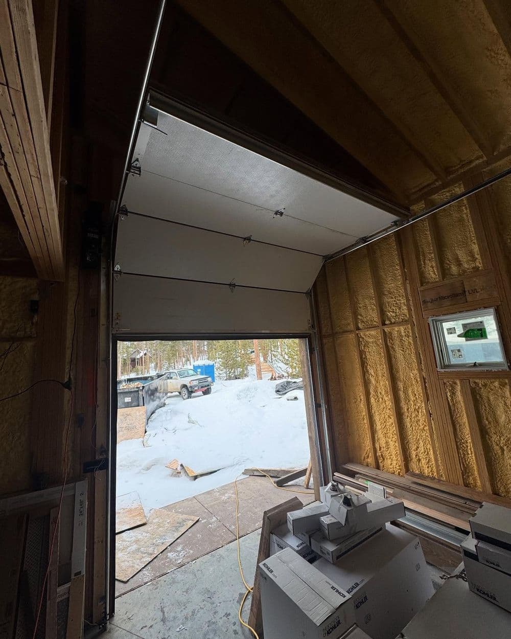 Interior view of a garage with a partially opened door, snow visible outside.
