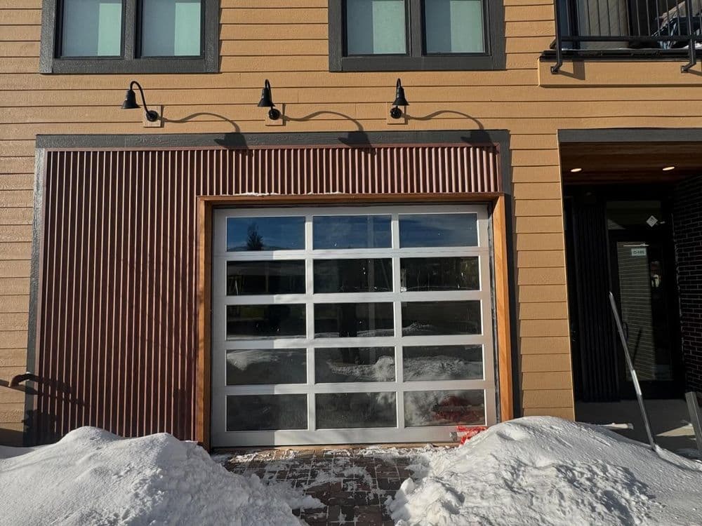 Modern garage door with wooden trim against a brown house, surrounded by snow.