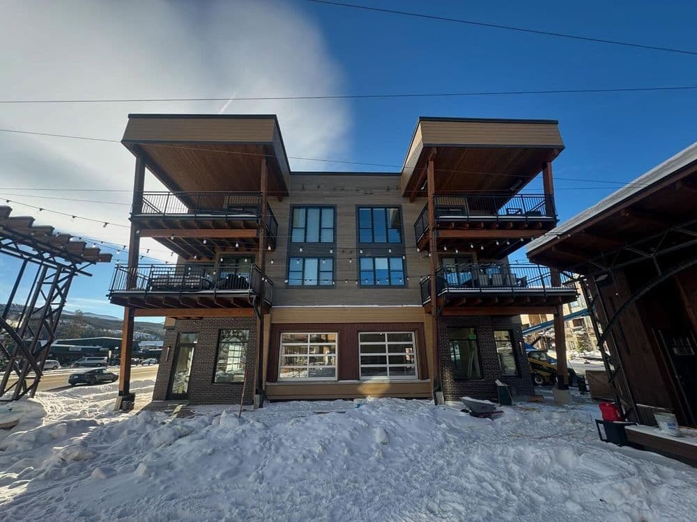 Modern three-story building with balconies, surrounded by snow and a clear blue sky.