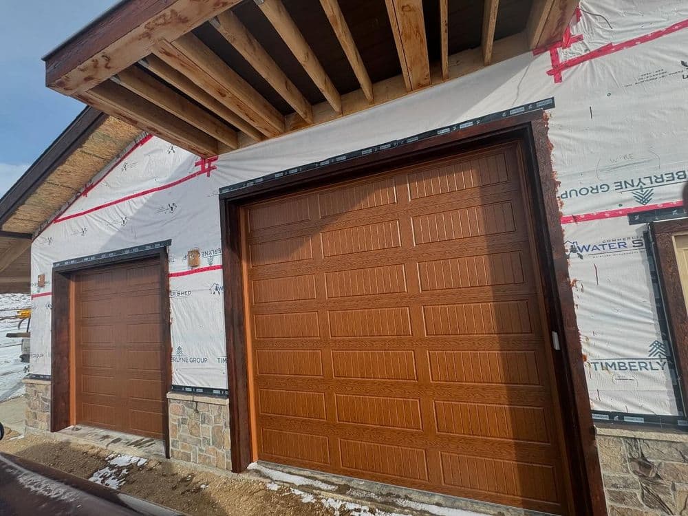 Modern brown garage doors on a newly constructed home with exterior wrapping and exposed framing.