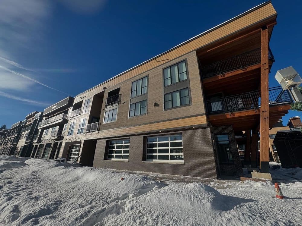 Modern wooden and brick apartment building with snow-covered ground under a clear blue sky.