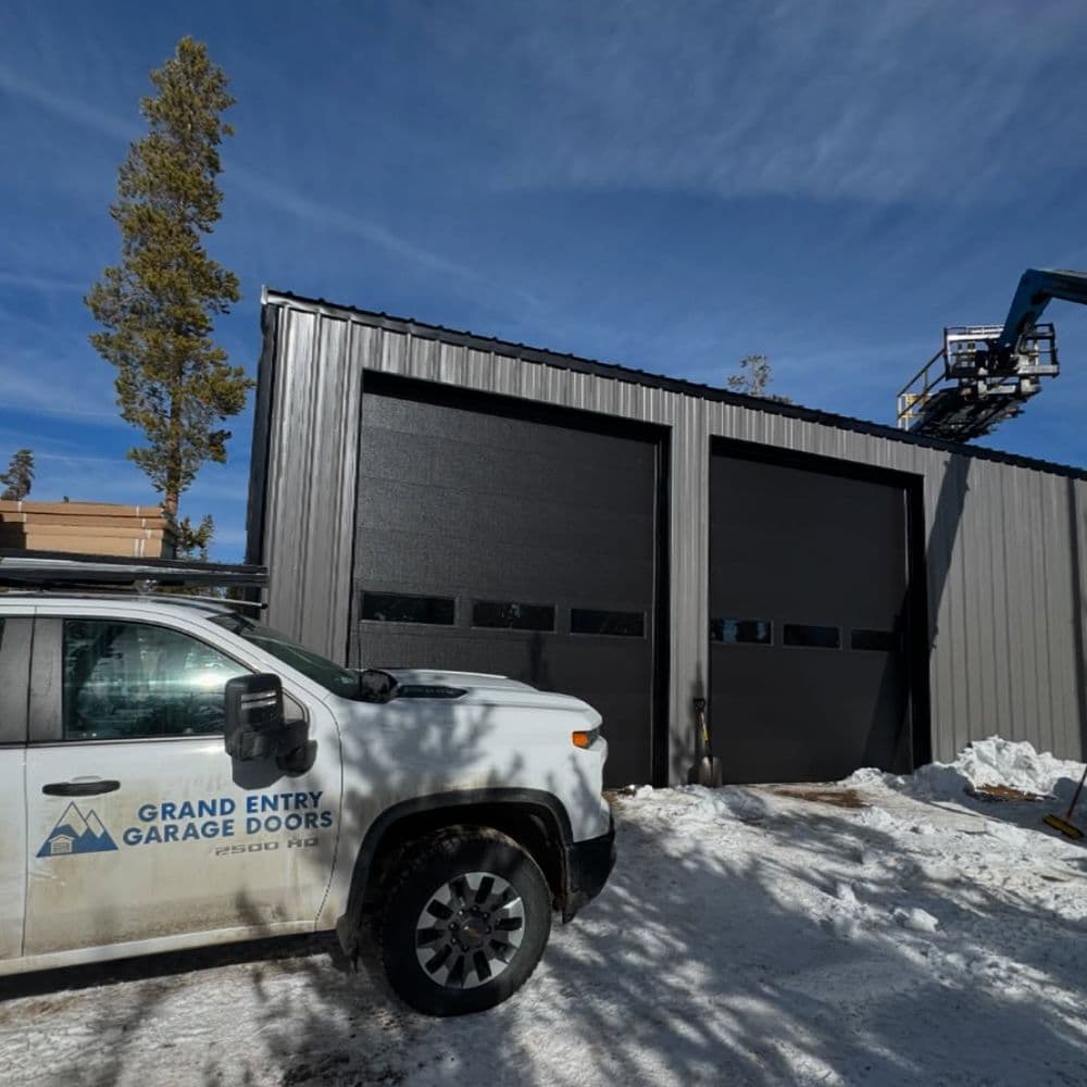 Grand Entry Garage Doors truck in front of a metal building with large doors in winter setting.